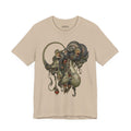 Front of Before the Light Returns T-Shirt in Tan, featuring an ornate olive and bronze creature with a curled tail.